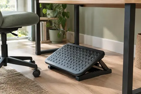 Repose-pieds noir réglable sous un bureau en bois clair, avec plateforme texturée et inclinaison mobile.