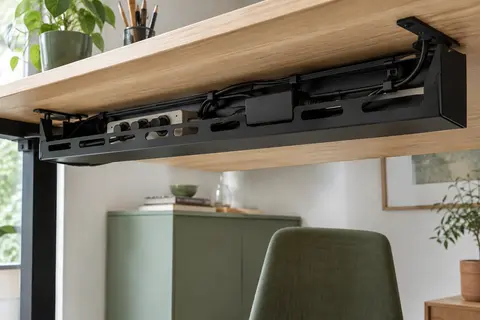 Goulotte en acier noir sous un bureau en bois clair, avec multiprise et câbles rangés.